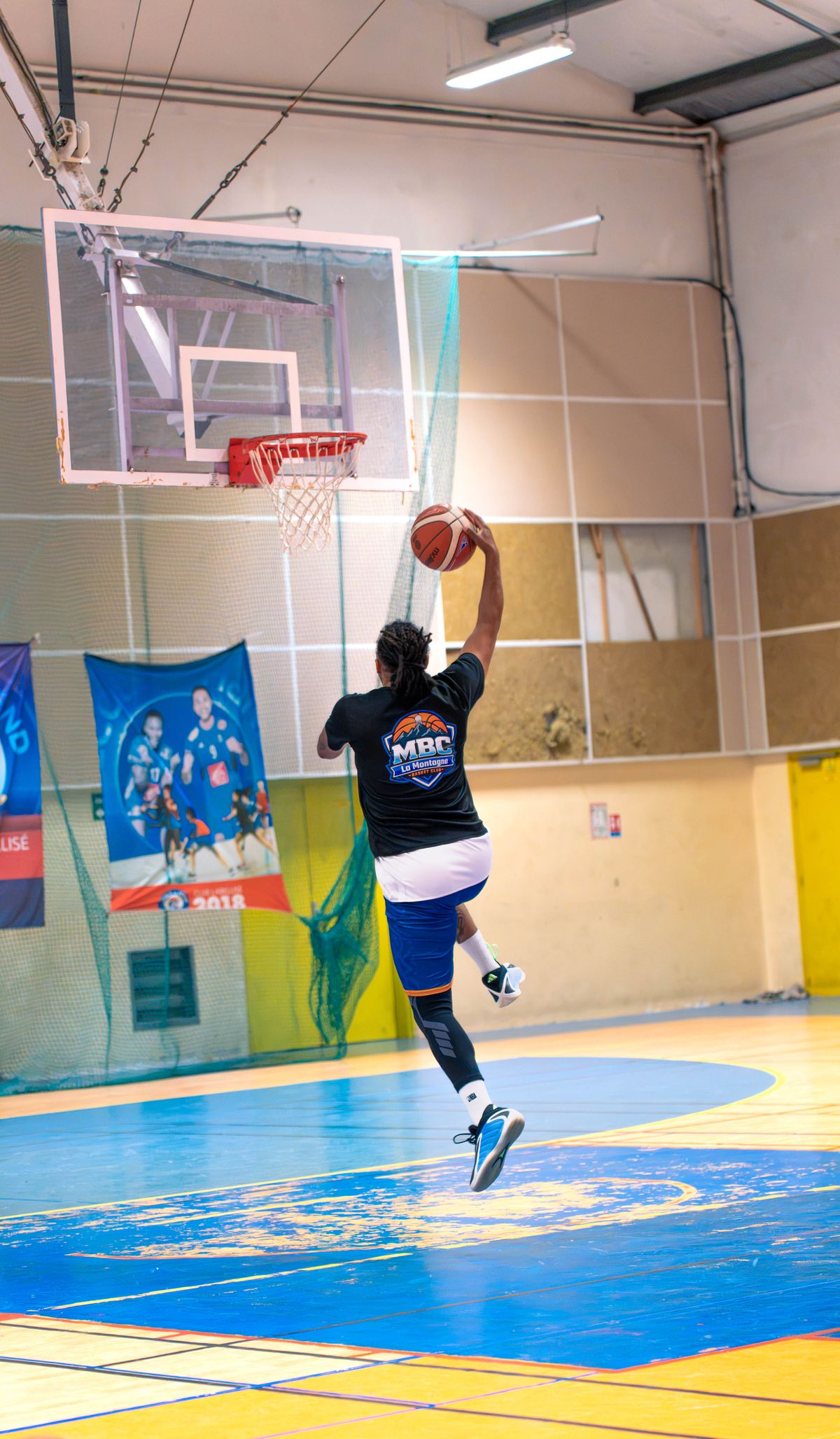 Échauffement au gymnase de La Montagne : un joueur du MBC en tee-shirt noir du club s'élève seul vers le cercle, le ballon tenu d'une main.