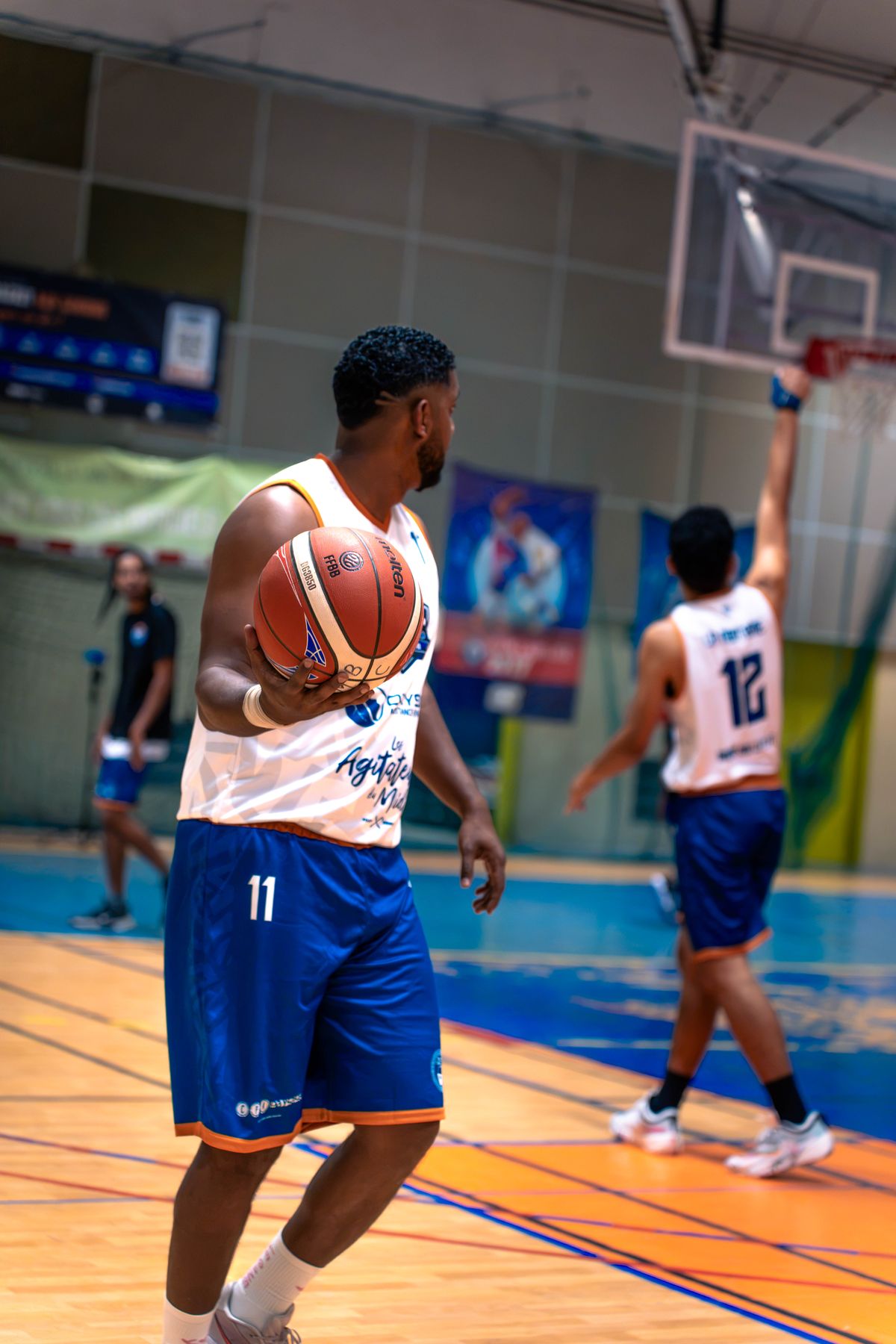 Le numéro 11 du MBC, ballon en main, en maillot blanc et short bleu ; derrière lui, le numéro 12 lève le bras sous le panier.