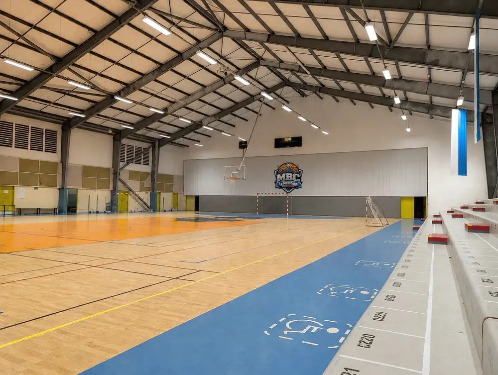 Intérieur du Gymnase de La Montagne, la salle du MBC, avec le logo du club au mur et le terrain de basket.