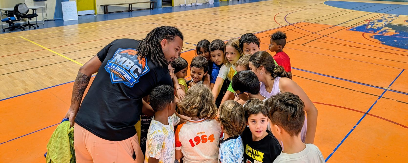 L'école de basket du MBC au gymnase de La Montagne : l'entraîneur, maillot du club sur le dos, rassemble une vingtaine d'enfants en cercle au bord du terrain avant l'entraînement.
